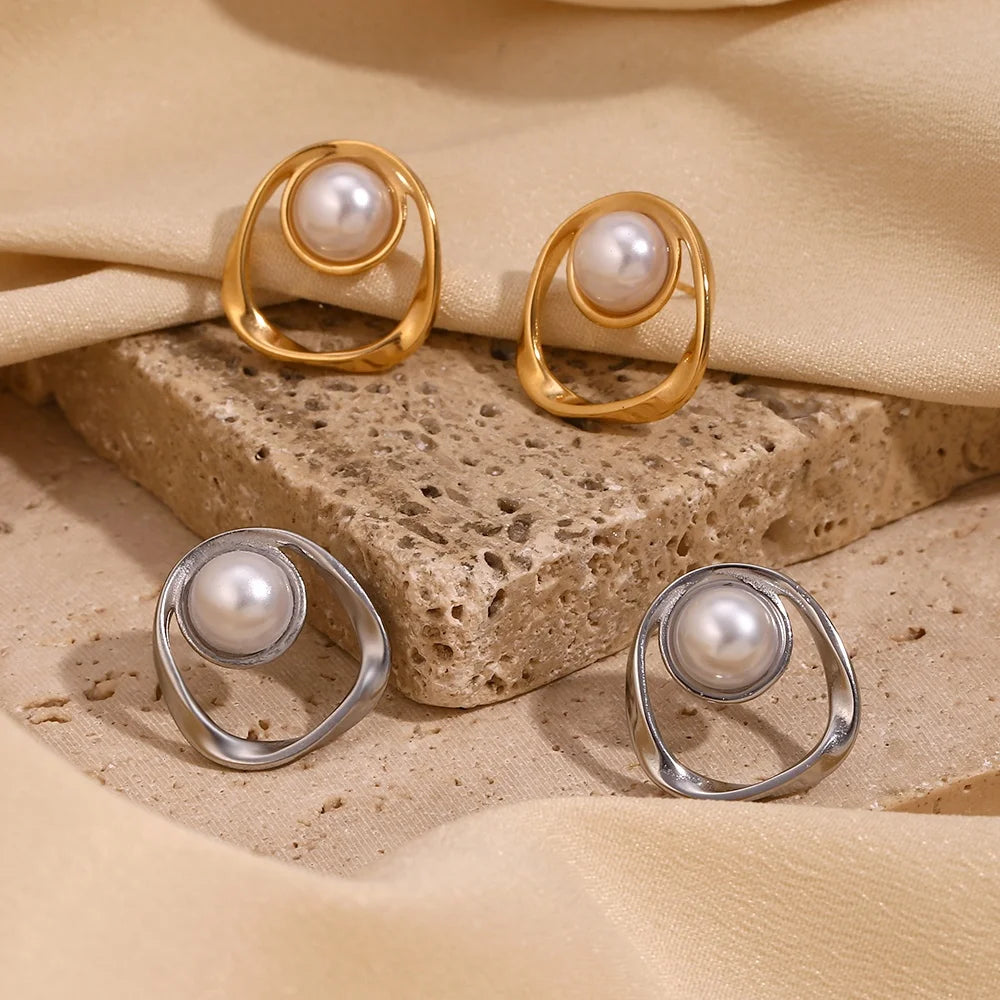 Pair of gold and silver earrings with pearls on a textured beige surface