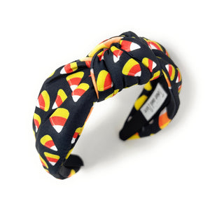 A black headband with colorful candy corn print, featuring white, orange, and yellow. Fun, Halloween-themed accessory.