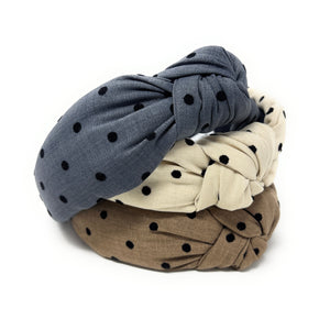Three fabric headbands with black polka dots are arranged in a triangular pattern. They are beige, tan, and charcoal blue, each with a knotted design, conveying a casual, stylish tone.