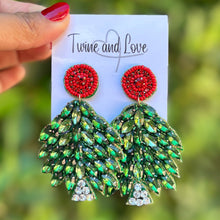 Load image into Gallery viewer, Hand holding a card with green and red earrings against a blurred green background