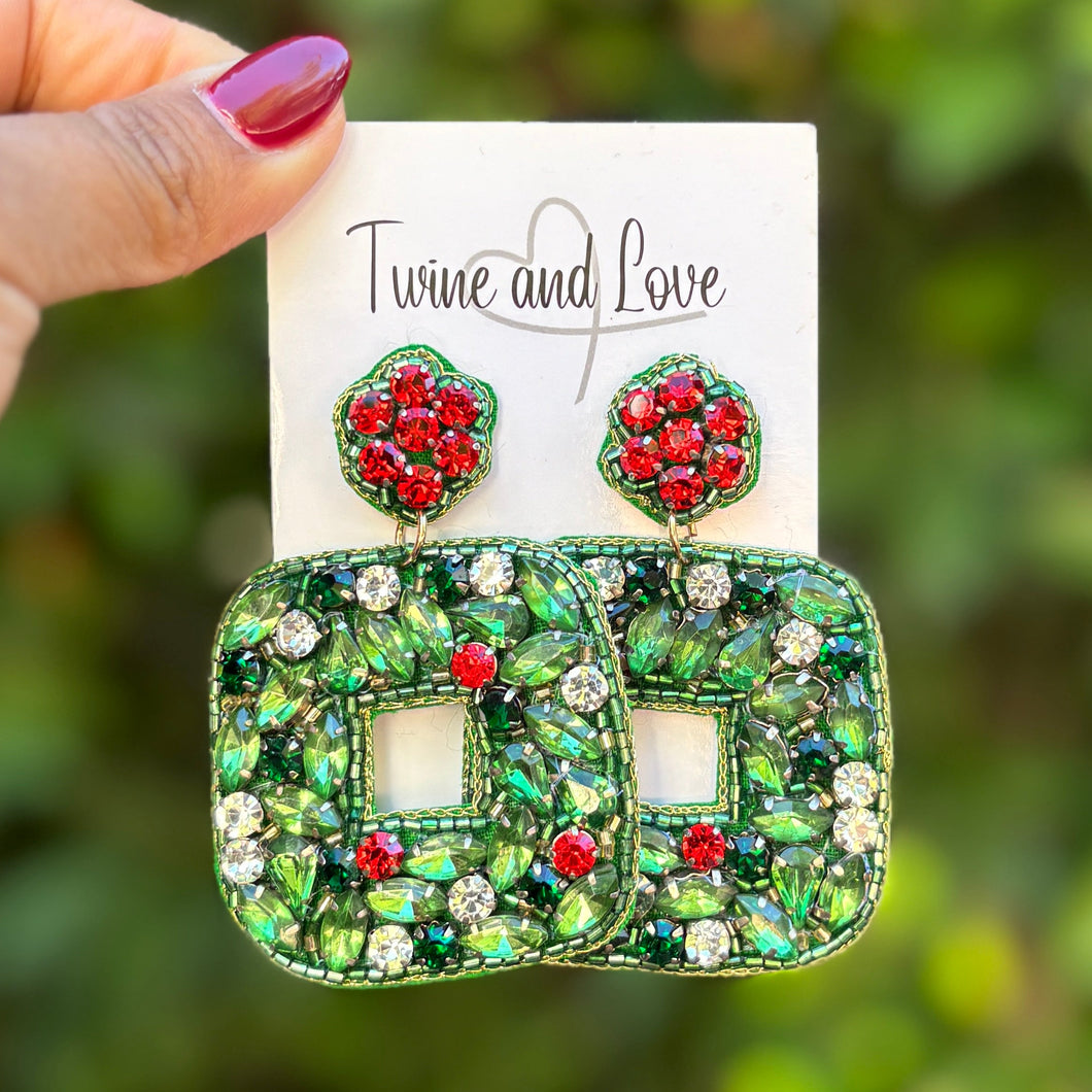 Green and red earrings held on a card with a blurred green background