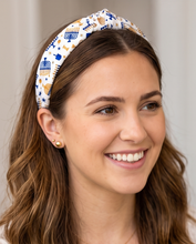 Load image into Gallery viewer, A smiling woman with wavy brown hair wearing a white fabric headband decorated with blue and gold menorah and star patterns, photographed in a clean indoor setting.