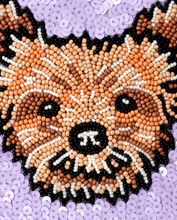 Load image into Gallery viewer, A close-up of a beaded dog face, showing a fox or cat-like face made from small round beads in black, white, tan, and brown, surrounded by lavender sequins.