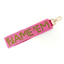 Load image into Gallery viewer, A pink beaded wristlet strap with the text 'NAME'EM' in green, attached to a metal D-ring.