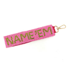 Load image into Gallery viewer, A pink beaded wristlet strap with the text 'NAME'EM' in green, attached to a metal D-ring.
