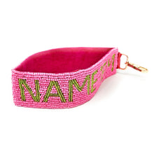 Load image into Gallery viewer, A pink beaded wristlet strap with the text 'NAME'EM' in green, attached to a metal D-ring.