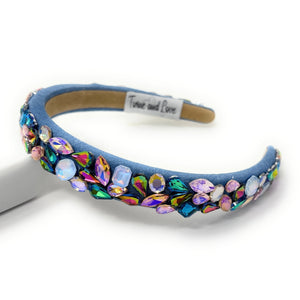 A vibrant, gemstone-encrusted headband with a blue fabric base adorned with multicolored jewels, including blue, purple, and gold, emanating a luxurious and playful vibe.