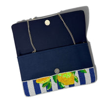 Load image into Gallery viewer, A navy blue fabric clutch bag with a gold-tone chain strap, featuring a decorative beaded lower border with blue and white stripes and yellow-green citrus motifs, shown on a white background.