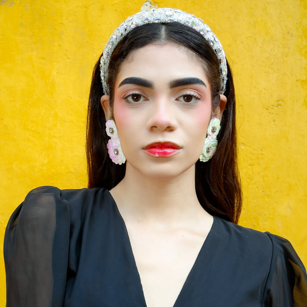 Woman wearing beautiful floral earrings with a black top with sheer sleeves against a yellow background