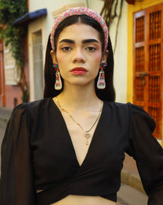 Woman wearing "It's My Birthday" earrings with a black top and white pants with jewelry outdoors.
