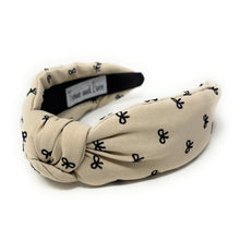 Load image into Gallery viewer, Ivory headband with a knotted design, featuring small black bow patterns. The inside tag reads &quot;Time and Love.&quot; The tone is stylish and elegant.