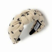 Load image into Gallery viewer, Ivory headband with a knotted design, featuring small black bow patterns. The inside tag reads &quot;Time and Love.&quot; The tone is stylish and elegant.