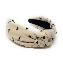 Load image into Gallery viewer, Ivory headband with a knotted design, featuring small black bow patterns. The inside tag reads &quot;Time and Love.&quot; The tone is stylish and elegant.