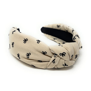 Ivory headband with a knotted design, featuring small black bow patterns. The inside tag reads "Time and Love." The tone is stylish and elegant.