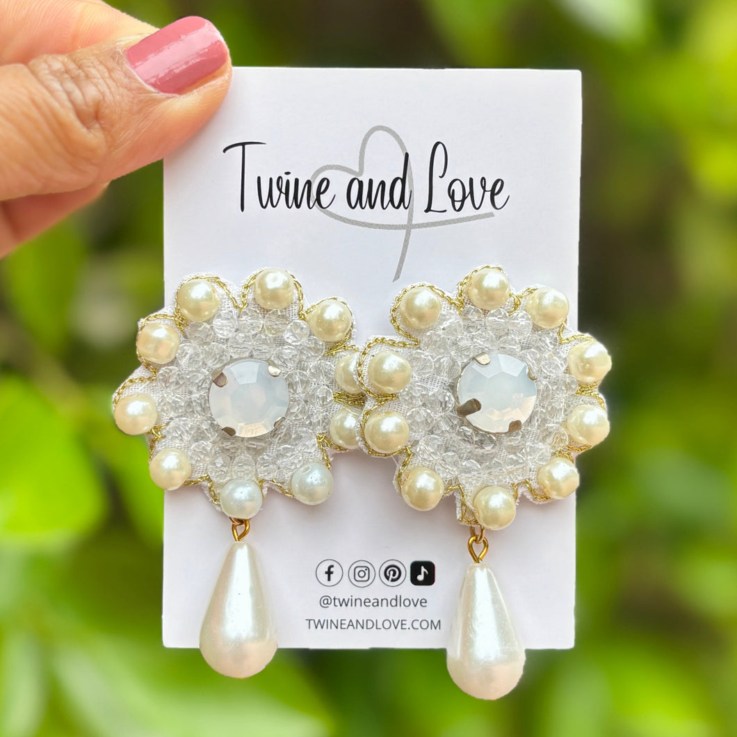 Elegant earrings feature clear beads surrounded by small pearls in a floral pattern, with a pearl teardrop dangling below, creating a classic, refined look.