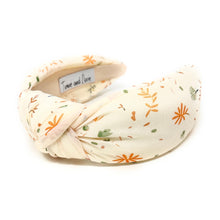 Load image into Gallery viewer, ivory-colored headband with a floral pattern in orange and green. It has a knotted design and visible label inside. Elegant and playful tone.