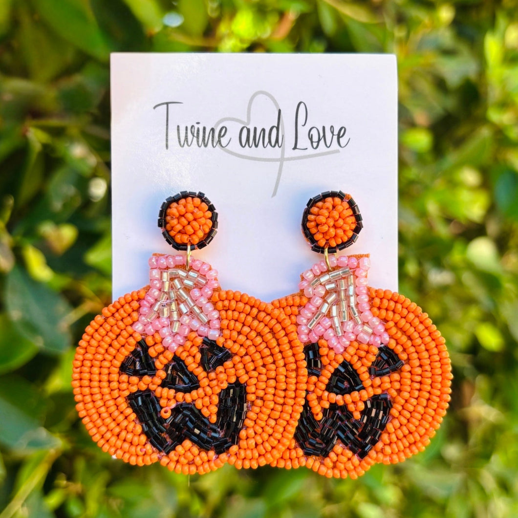 Pumpkin-shaped beaded earrings on a card with 'Twine and Love' branding, against a green leafy background.