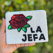Load image into Gallery viewer, Hand holding a beaded pouch with a rose and 'LA Jefa' text against a blurred green background