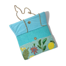 Load image into Gallery viewer, A turquoise blue fabric clutch bag with a gold-tone chain strap, featuring a decorative embroidered border with green leaves, yellow lemons, and a red flower on a white background.