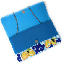Load image into Gallery viewer, A bright blue fabric clutch bag with a beaded border featuring yellow lemons and navy blue scrollwork, complete with a silver-tone chain strap and snap button closure.