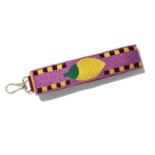 Load image into Gallery viewer, A purple woven keychain strap featuring a yellow and green beaded lemon design, with a gold metal lobster clasp on a white background.