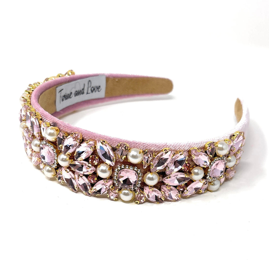 Pink jeweled headband adorned with sparkling pink gemstones and pearls on a soft pink fabric. Elegant, luxurious, and feminine design.