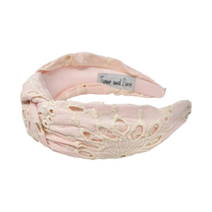 Pink headband with intricate white floral embroidery, displayed in a side view. The soft texture and elegant design convey a stylish, timeless appeal.