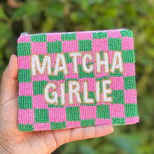 Load image into Gallery viewer, A hand holding a small square beaded pouch with a pink and green checkered pattern and the words 'MATCHA GIRLIE' in white beads, set against a blurred green outdoor background.