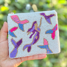 Load image into Gallery viewer, A hand holds a small square beaded clutch bag featuring colorful mermaid and fish motifs on a light beige background, with a blurred green outdoor background.