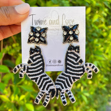Load image into Gallery viewer, Elegant woman wearing a black pearl-embellished knotted headband and zebra-shaped beaded statement earrings against a white backdrop.