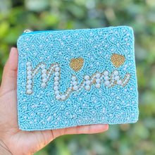 Load image into Gallery viewer, A hand holding a small turquoise glitter pouch with 'Mimi' and two hearts embroidered in white beads and gold thread, set against a blurred green foliage background.