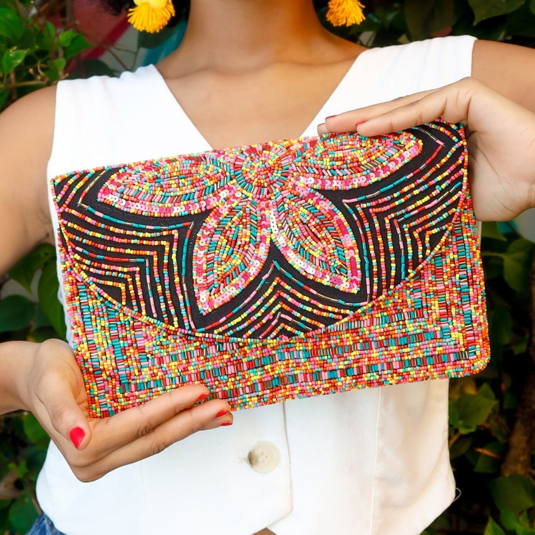 Woman holding a colorful beaded clutch against a green leafy background