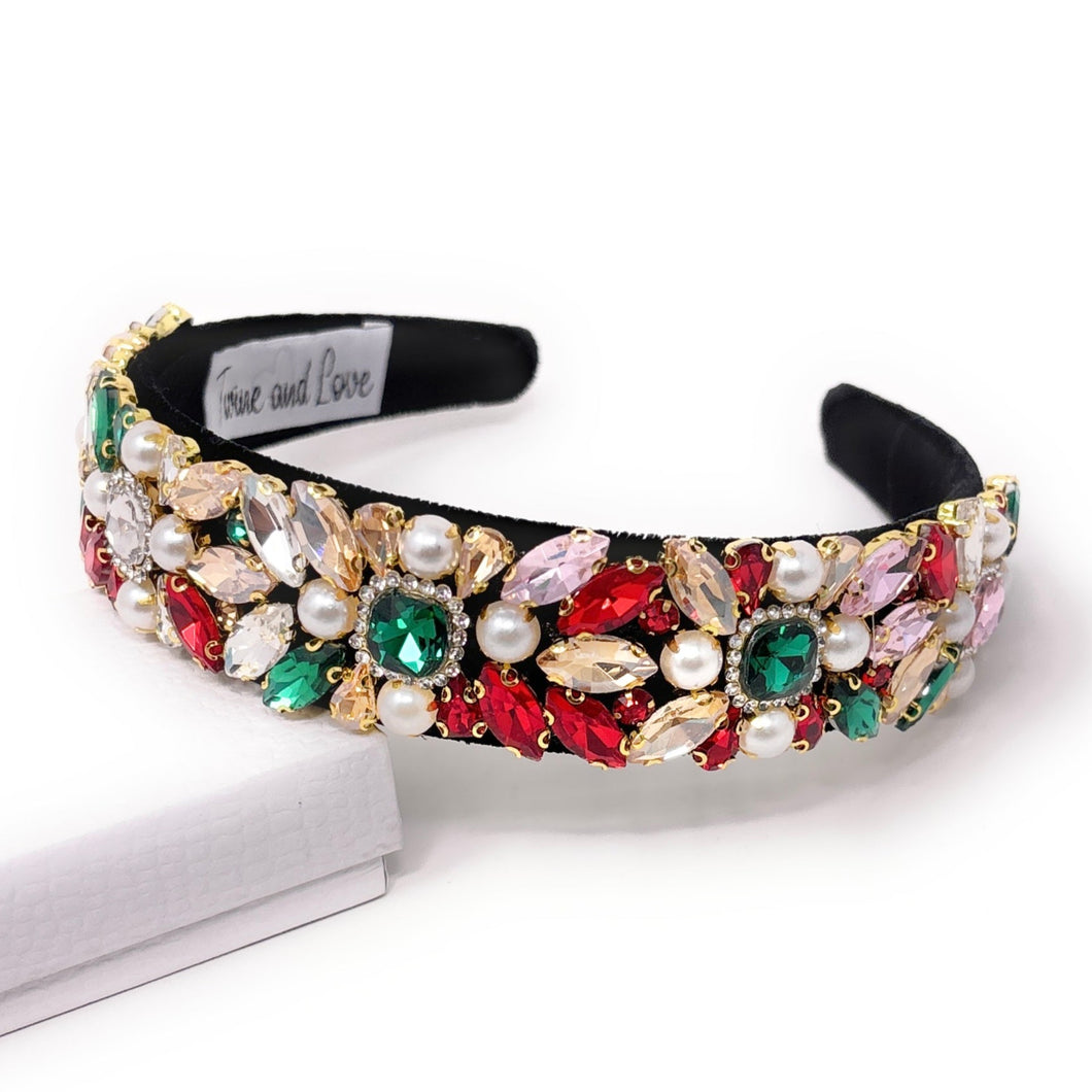 A jeweled headband with colorful gems in red, green, and pink, adorned with pearls on a black base, exudes an elegant and luxurious feel.