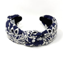 Load image into Gallery viewer, Navy blue headband with intricate white floral embroidery, displayed in a side view. The soft texture and elegant design convey a stylish, timeless appeal.