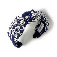 Load image into Gallery viewer, Navy blue headband with intricate white floral embroidery, displayed in a side view. The soft texture and elegant design convey a stylish, timeless appeal.