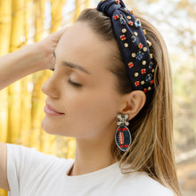 Load image into Gallery viewer, Woman wearing a navy headband with colorful embellishments and matching earrings against a blurred natural background.
