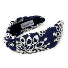 Load image into Gallery viewer, Navy blue headband with intricate white floral embroidery, displayed in a side view. The soft texture and elegant design convey a stylish, timeless appeal.