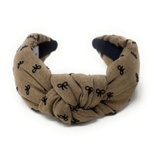 Load image into Gallery viewer, Neutral beige headband with a knotted design, featuring small black bow patterns. The inside tag reads &quot;Time and Love.&quot; The tone is stylish and elegant.