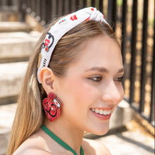 Load image into Gallery viewer, Fashion model wearing a novelty nurse-inspired headband paired with bold red statement earrings in sunlight.