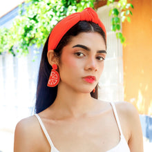 Load image into Gallery viewer, Colorful beaded orange slice dangle earrings held against green background
