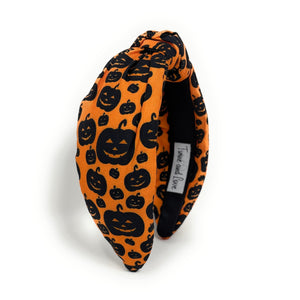 Orange knotted headband with black Halloween-themed prints, featuring pumpkins and cats. The design is playful, capturing a festive Halloween vibe.