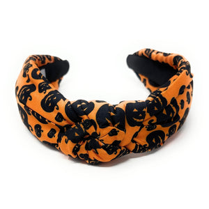 Orange knotted headband with black Halloween-themed prints, featuring pumpkins and cats. The design is playful, capturing a festive Halloween vibe.