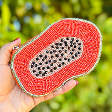 Load image into Gallery viewer, Hand holding a papaya shaped beaded  pouch against a blurred green background