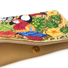 Load image into Gallery viewer, Close-up of a tan fabric clutch bag with a flap featuring colorful embroidered birds and tropical leaves, secured by a gold-tone snap button.