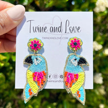 Load image into Gallery viewer, Fashion portrait of a woman wearing a pastel floral embellished headband and colorful tropical bird statement earrings outdoors.