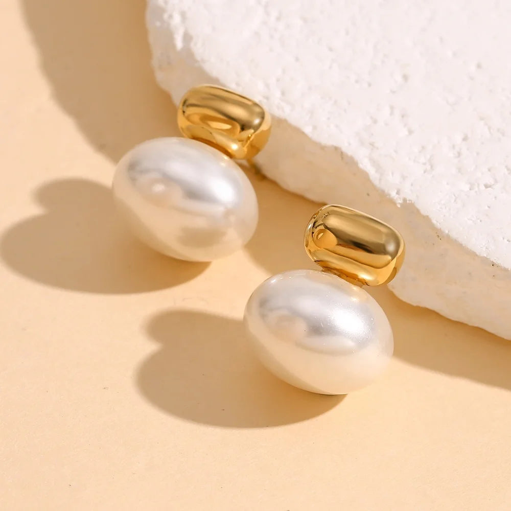 Pearl earrings with 18k gold plated accents on a textured beige surface