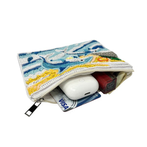 Beaded pouch featuring two blue dolphins jumping over stylized ocean waves. Background includes a yellow sun with spirals and green hills.