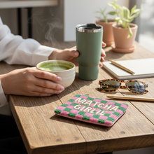 Load image into Gallery viewer, A cozy cafe-style scene with a person holding a green travel tumbler and a small bowl of matcha green tea at a wooden table. A pink and green checkered pouch with the words 'MATCHA GIRLIE' sits on the table, along with sunglasses, a notebook, and potted plants in the background.