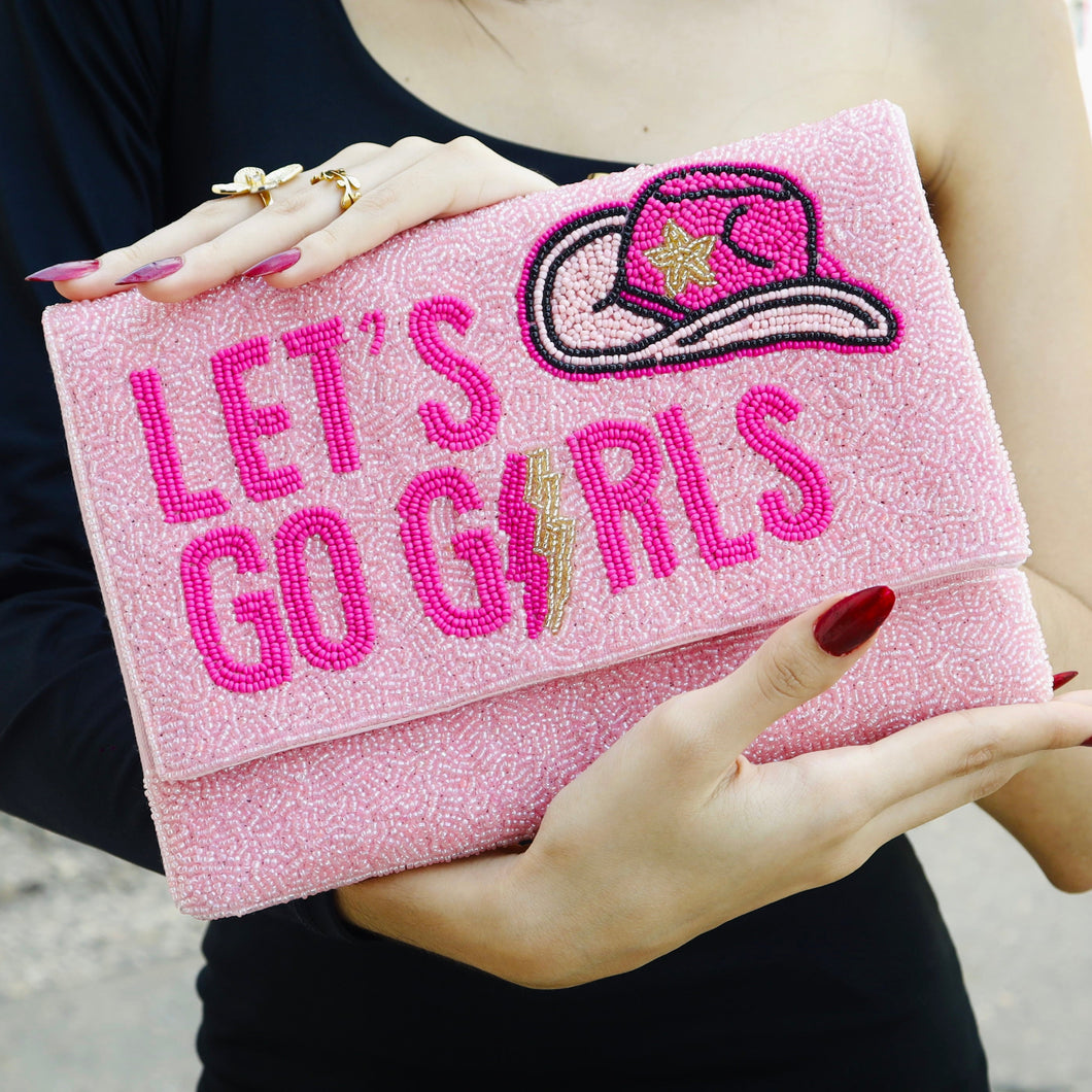 Pink clutch bag with 'Let's Go Girls' text and embroidered design held by a person.