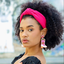 Load image into Gallery viewer, Curly-haired model showcasing a bright pink turban-style headband paired with a chic black dress.